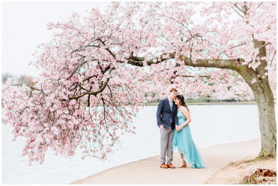 Couple standing under a cherry blossom tree by the water
