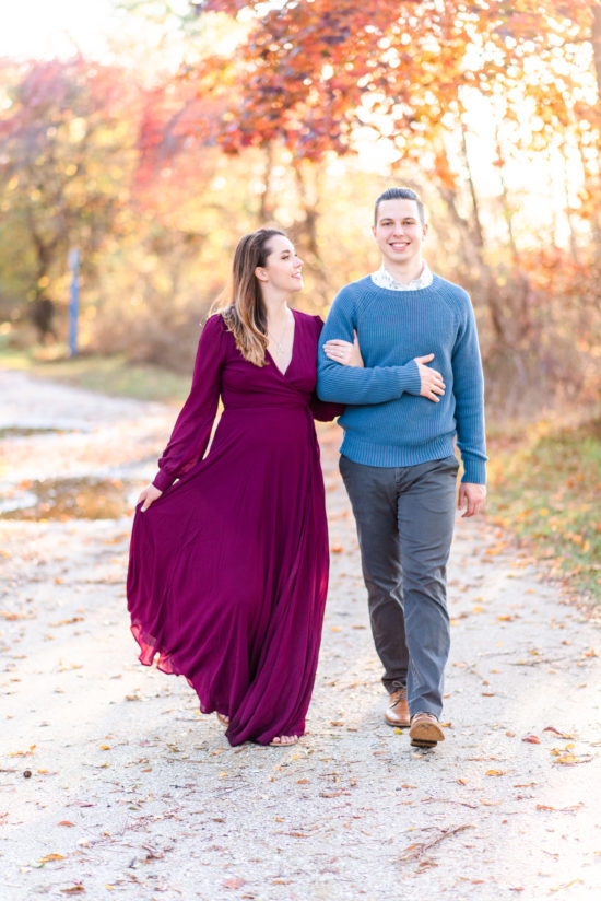 Fall Maryland Beach Engagement Session. Se is wearing a purple floor length flowing gown, and he is wearing a blue sweater as they walk towards the camera