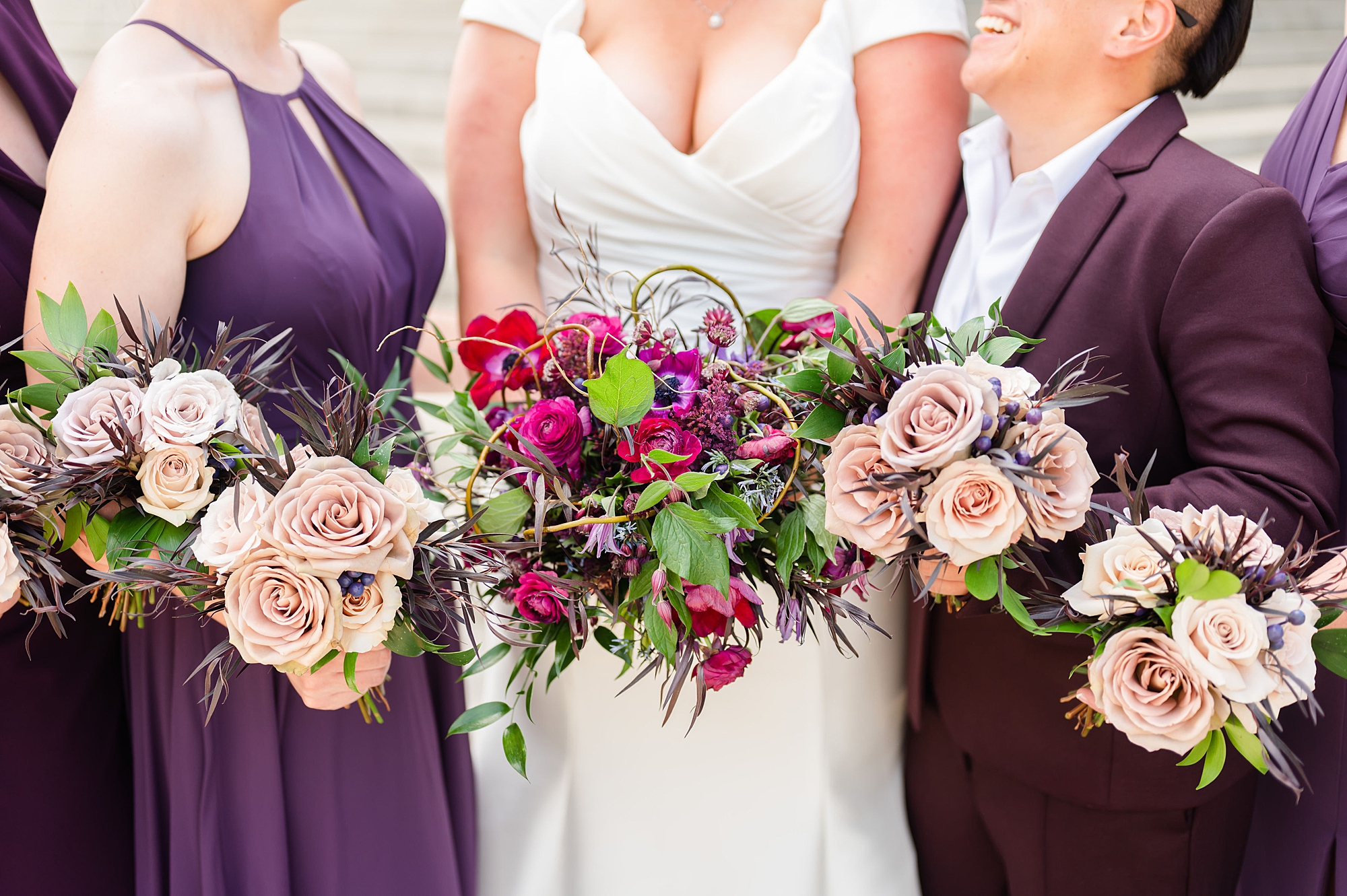 bride stands with wedding party in plum with bright bouquets 