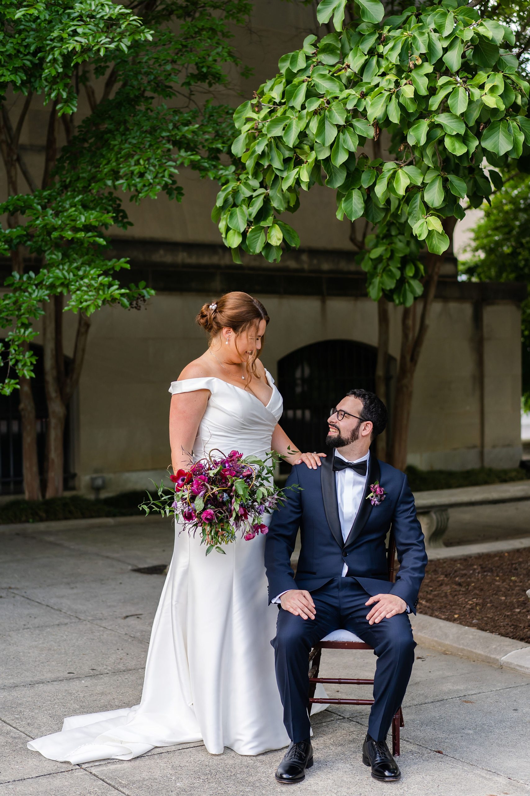 bride looks down at groom sitting in chair at Baltimore Museum of Art
