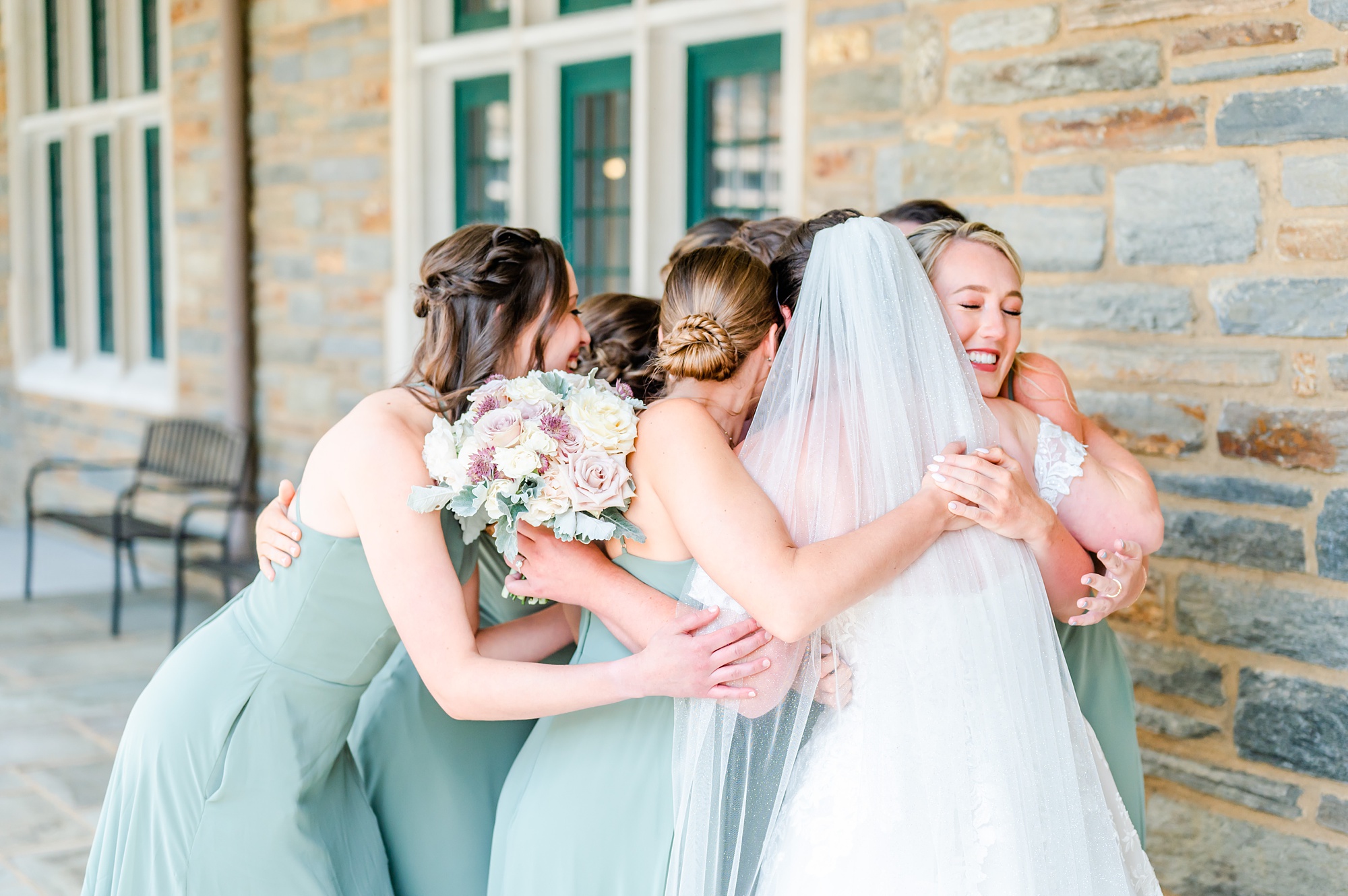 bridesmaids in sage green hug bride at Saint Andrews School