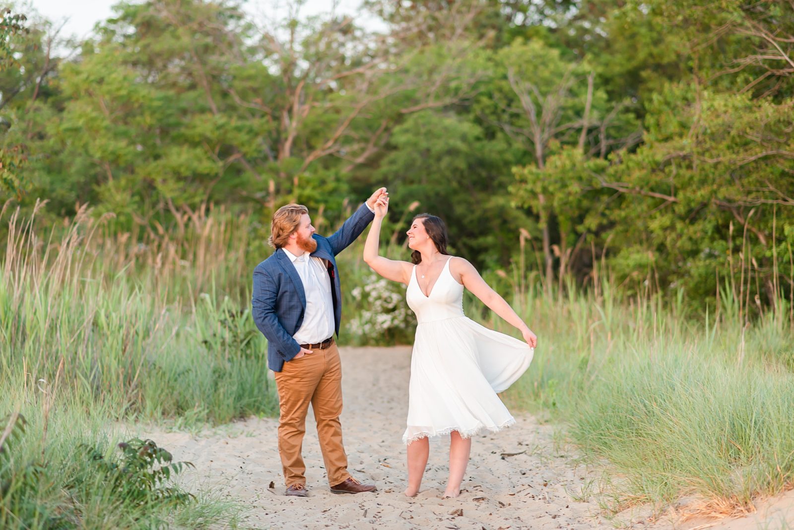 groom in blue suit jacket twirls bride in white dress during engagement photos 