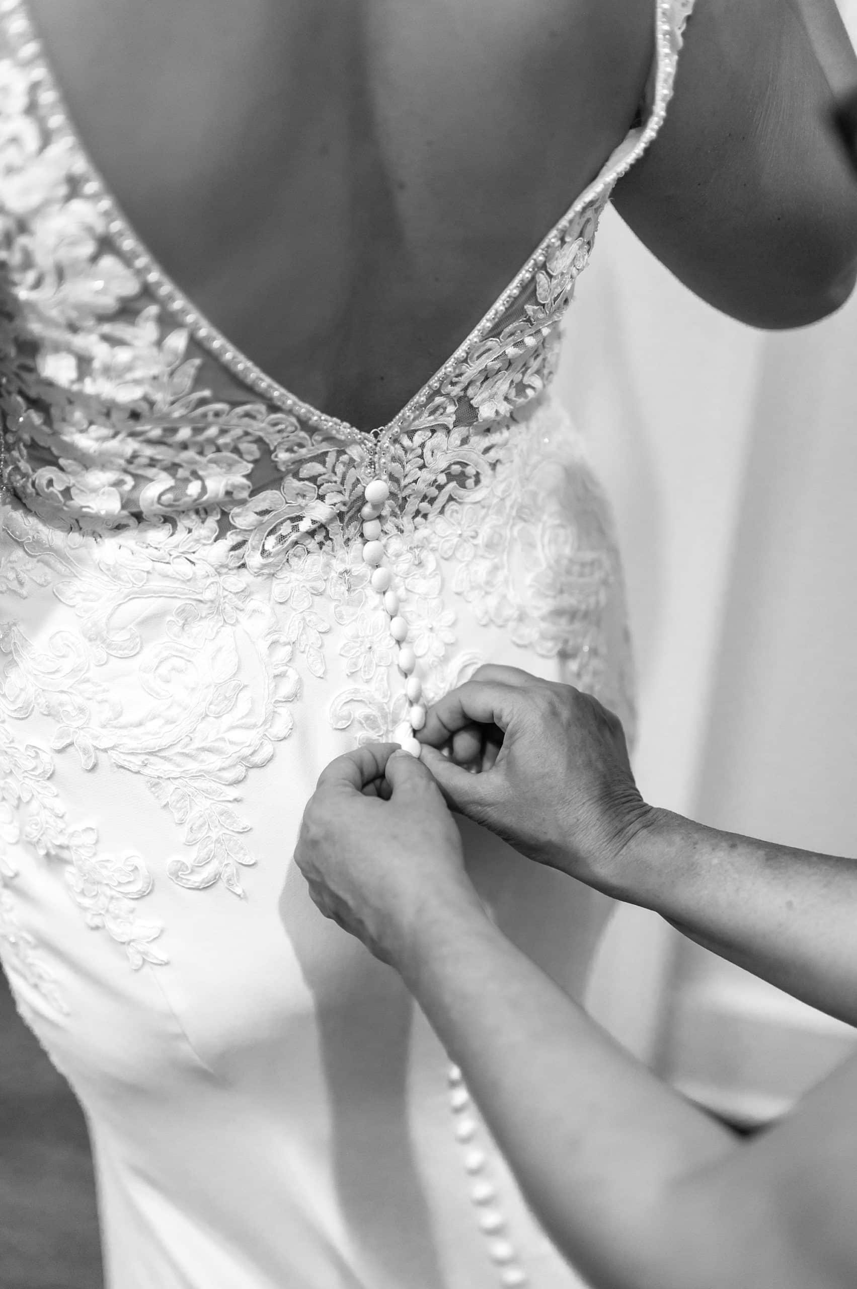 woman helps button up bride's wedding dress