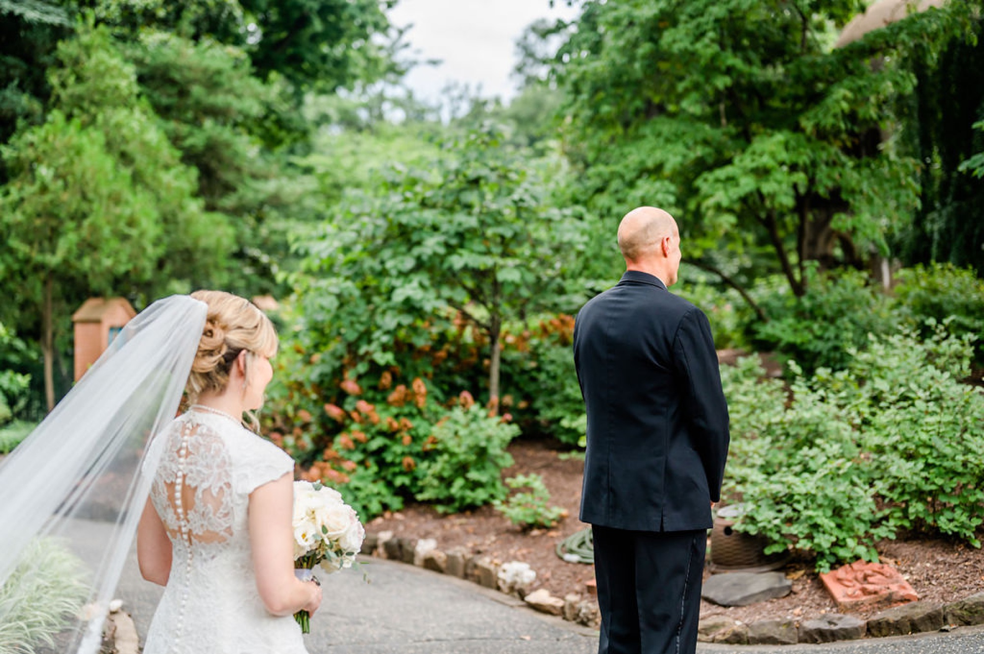 bride approaches groom for first look at Saint Francis Hall gardens