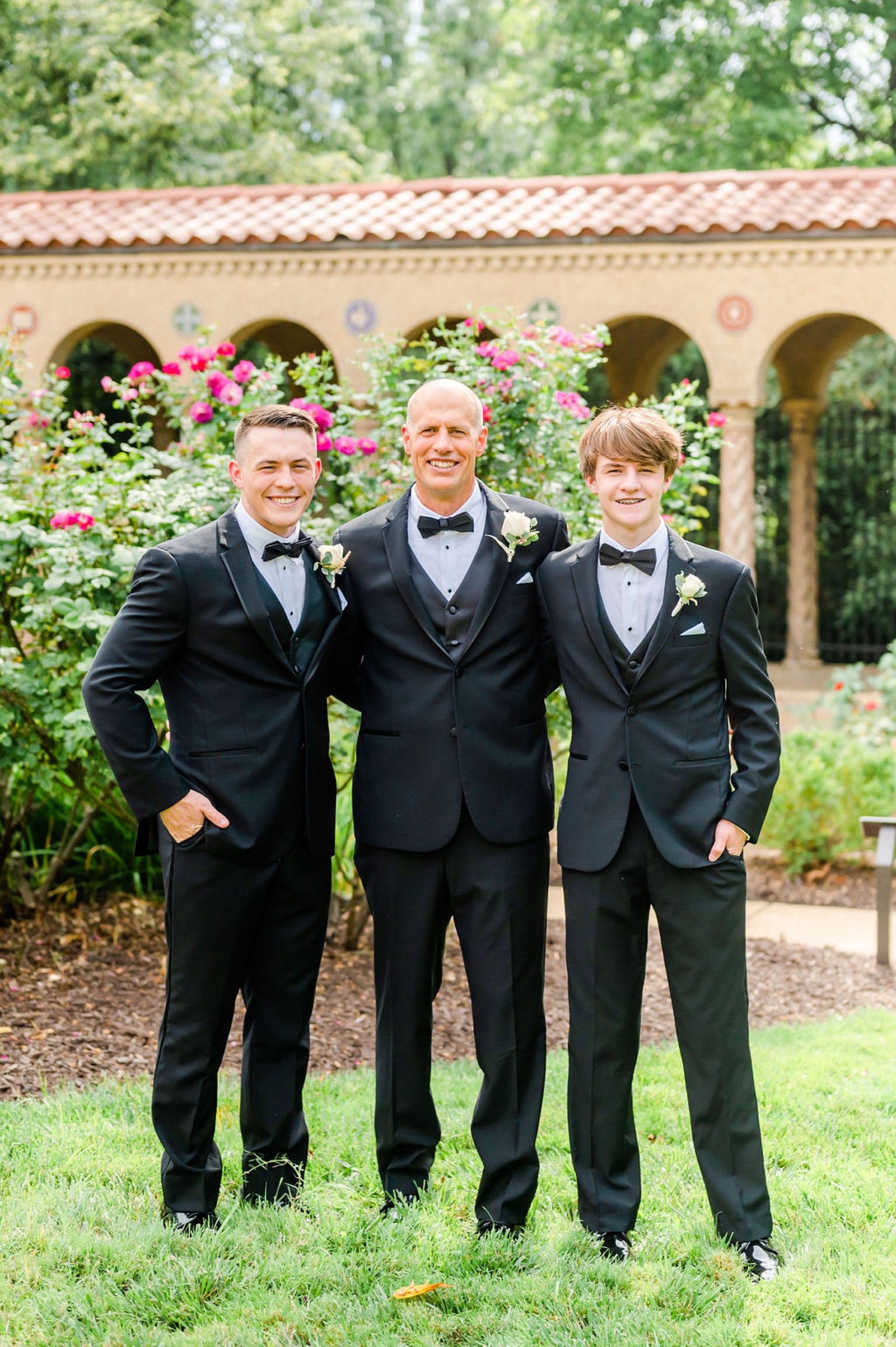 groom stands with sons in courtyard at Saint Francis Hall in tuxes 
