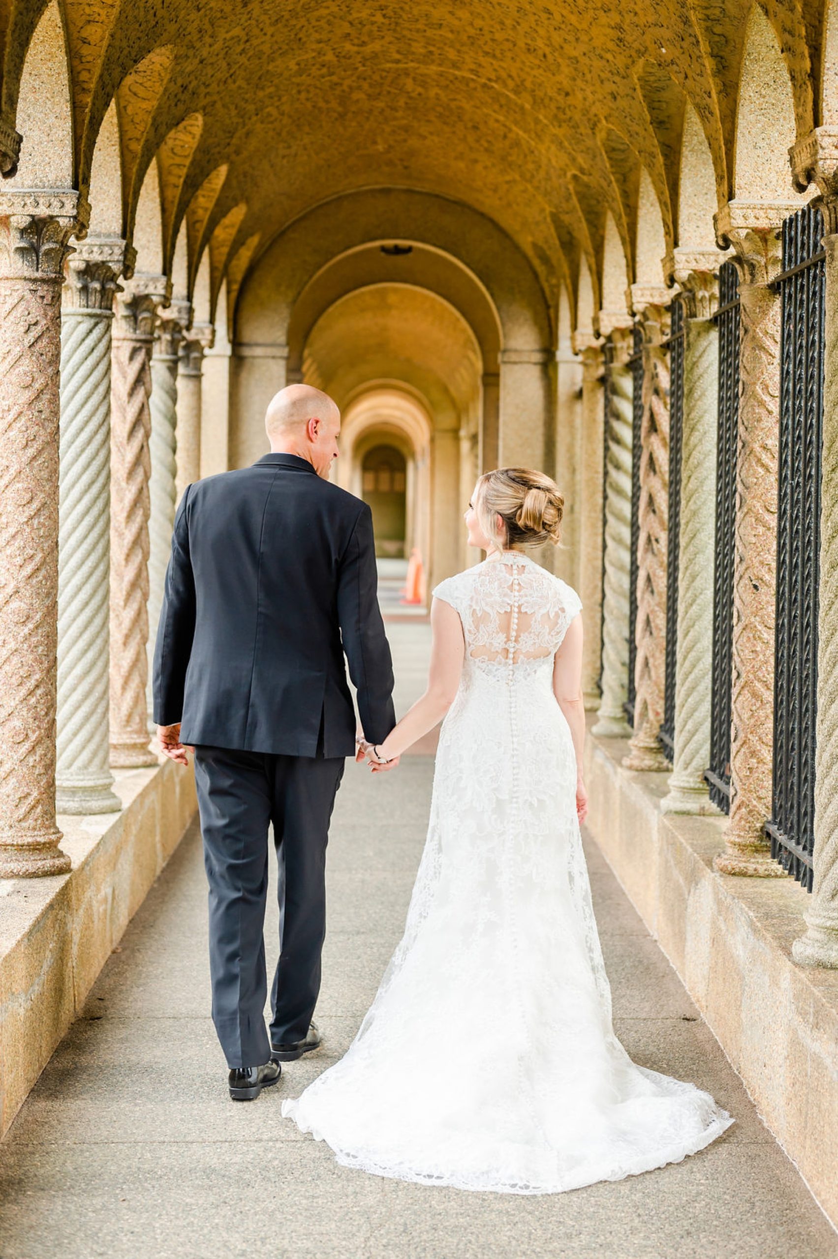 bride and groom hold hands down outside hallway at Saint Francis Hall