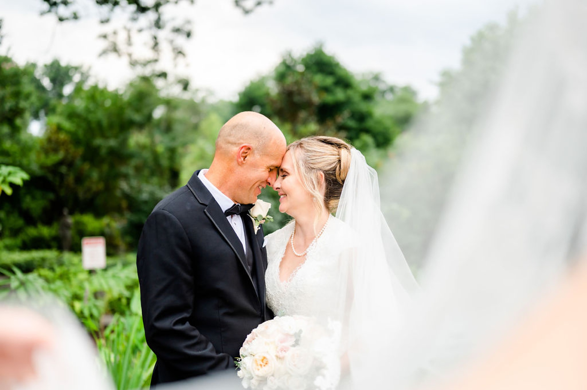 bride and groom lean head together with bride's veil floating