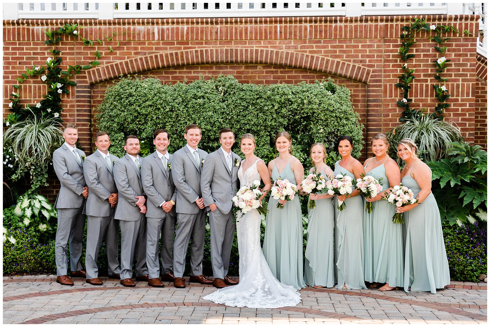 newlyweds stand with wedding party in grey and sage green