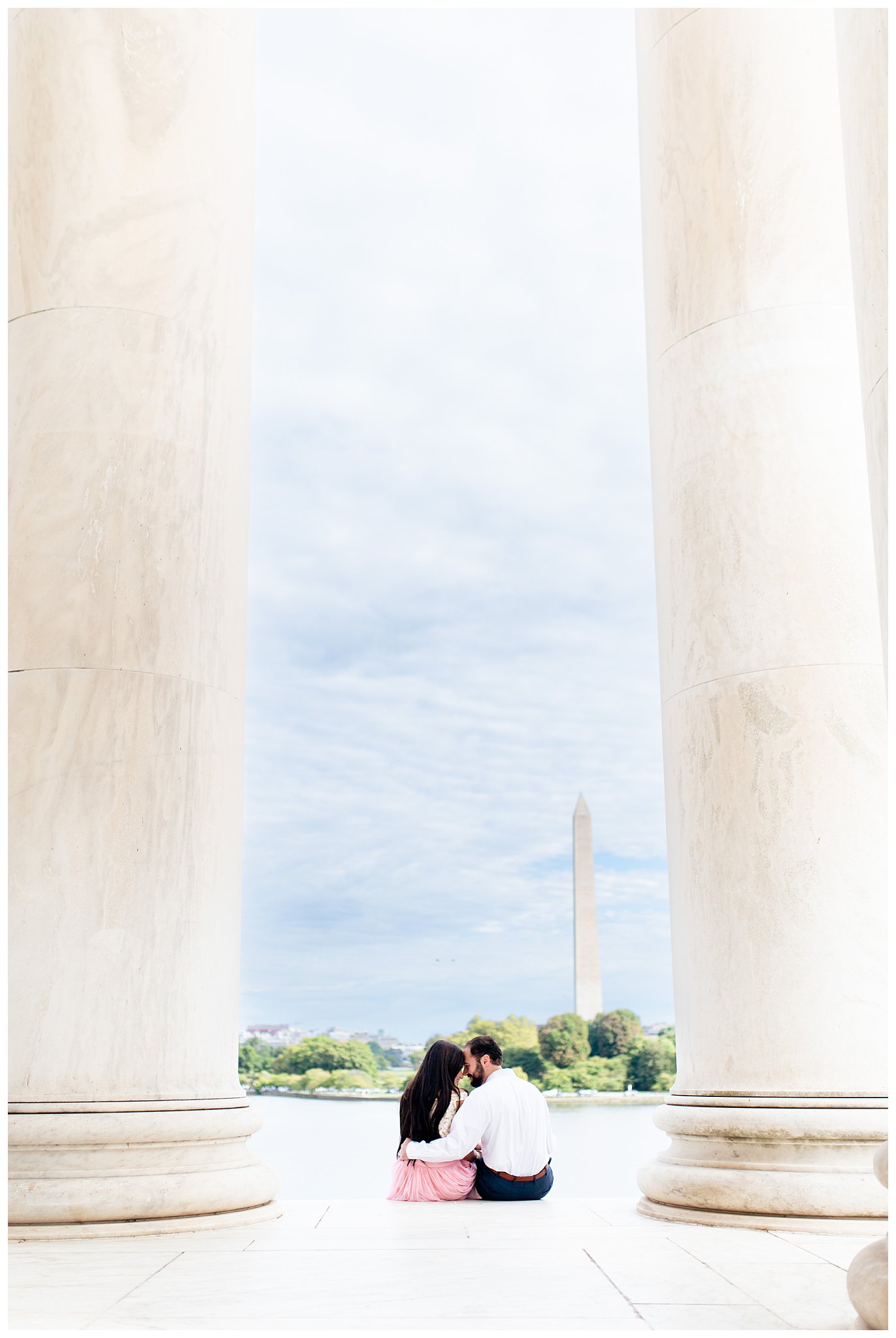 engaged couple sits on steps of Jefferson Memorial looking at Washington Monument