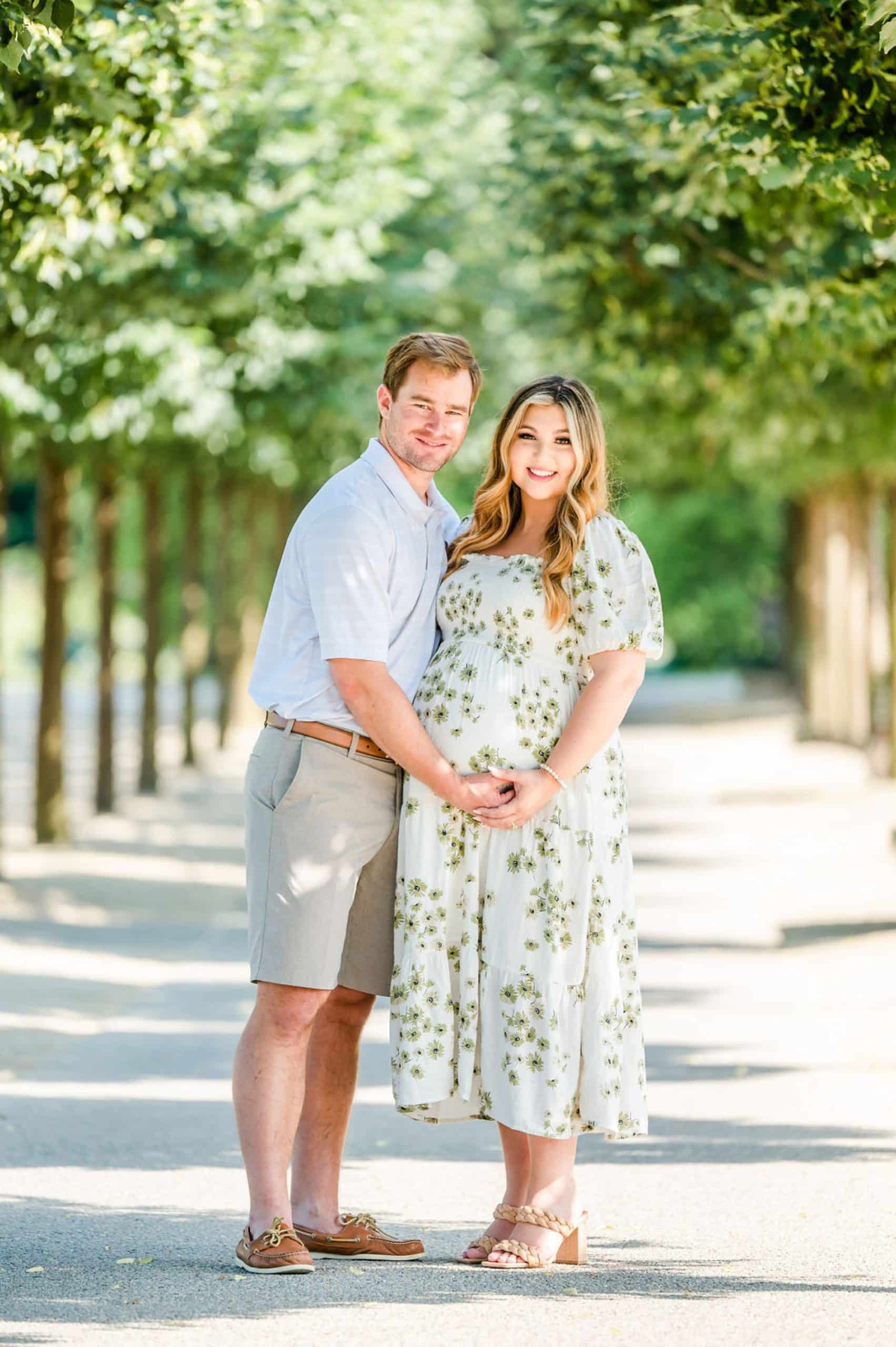 husband and wife pose on pathway at Longwood Gardens during maternity portraits 