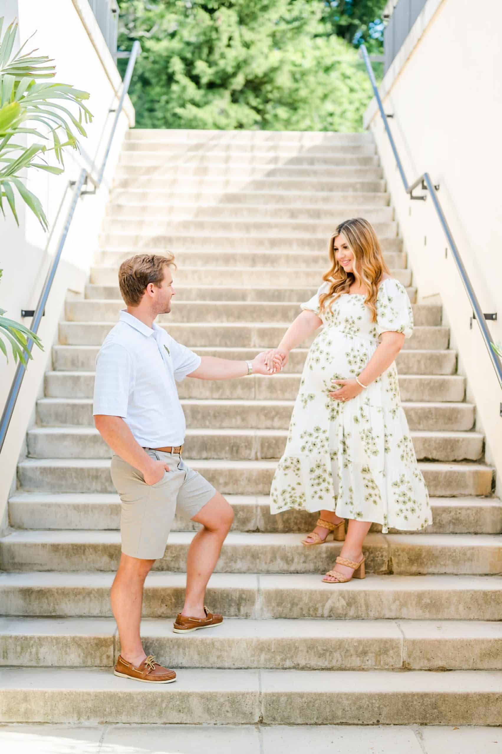 husband leads expecting wife down steps during maternity portraits at Longwood Gardens