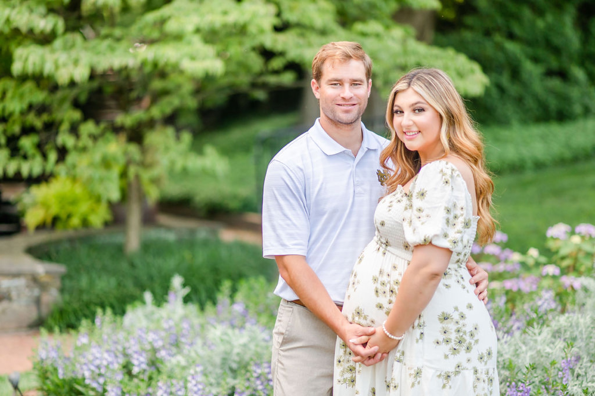 married couple holds hands standing in Longwood Gardens during maternity session