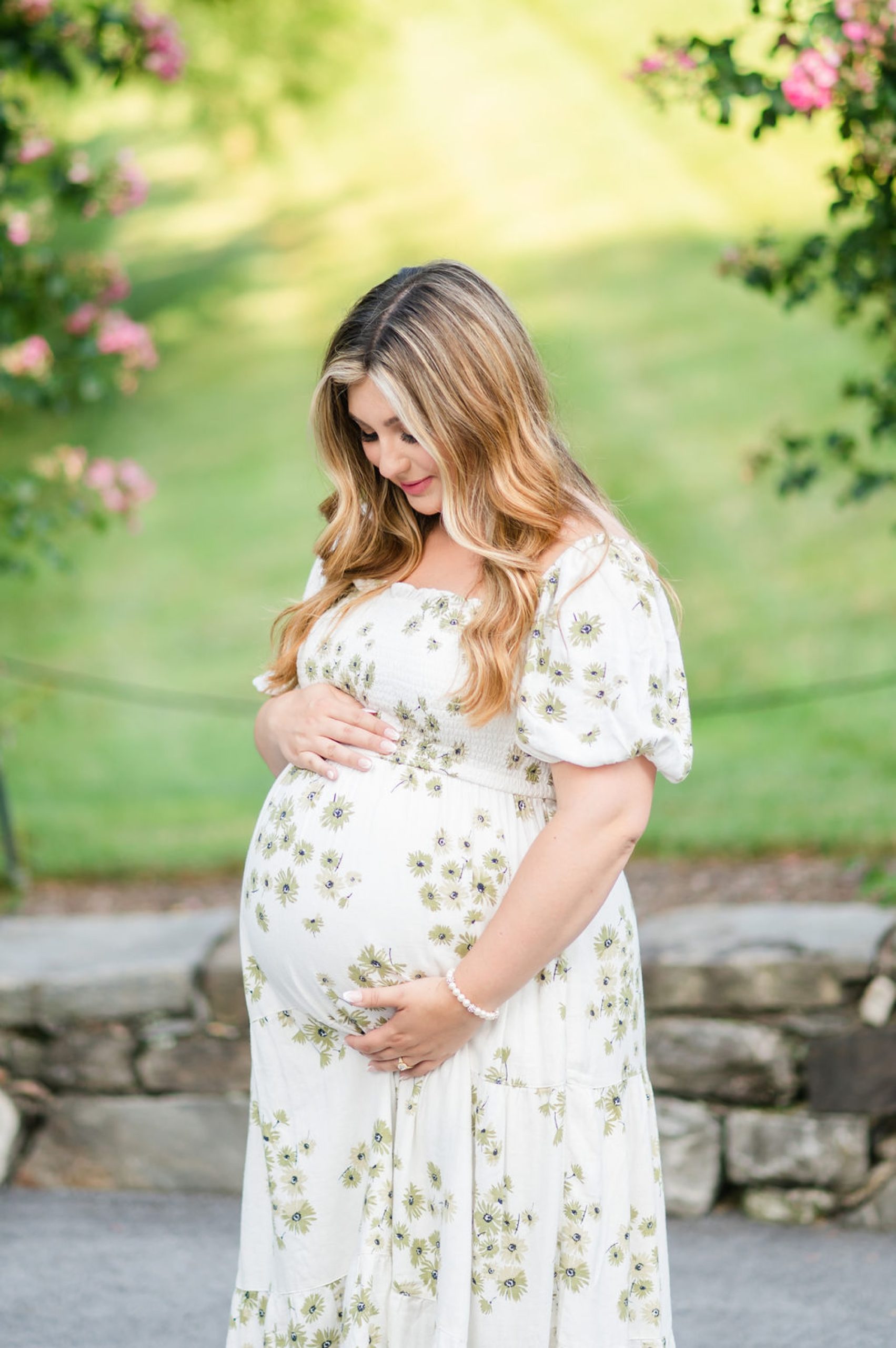 expecting mother looks down at bump wearing green and white dress