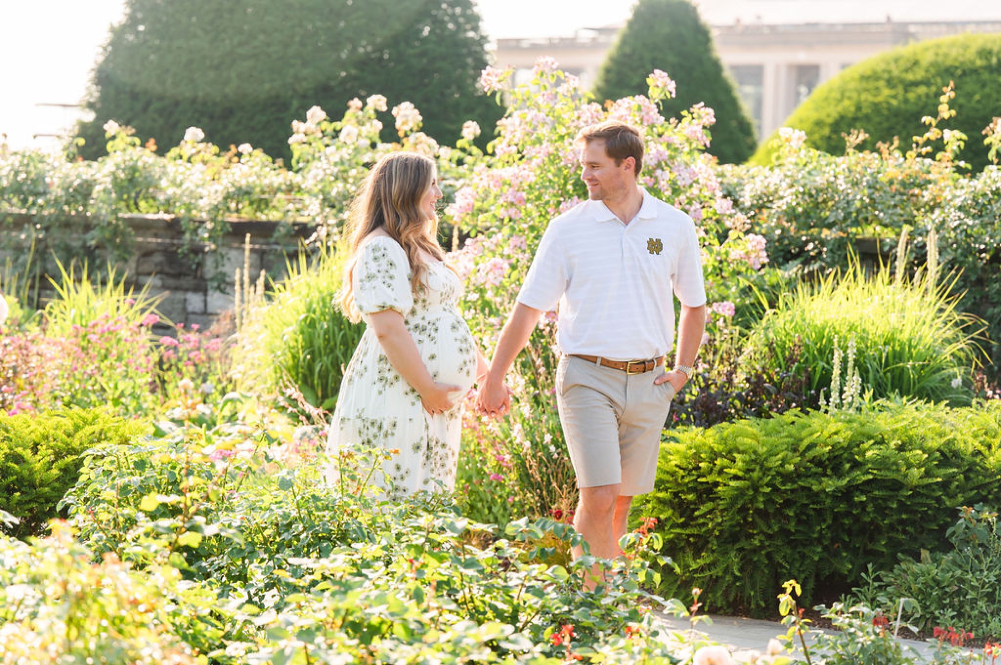 couple holds hands walking through garden during maternity session 