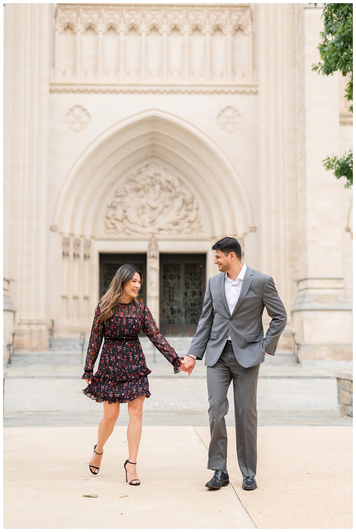engaged couple holds hands outside white walls of National Cathedral
