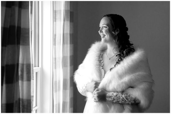 Bride stands in fur shaw looking out window