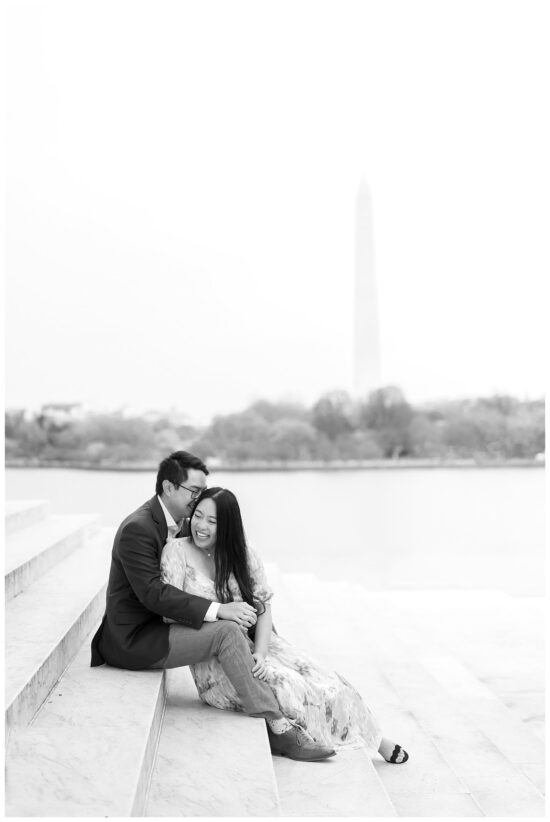 Black and white of couple sitting on steps with Washington Monument behind them