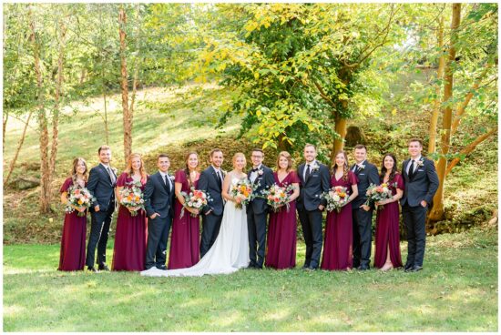 Wedding party stands in in a field under fall trees
