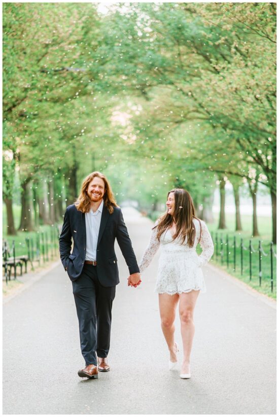 Couple walking down a tree lined pathway laughing at eachother