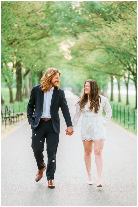 Couple walking down a tree lined pathway towards the camera. 